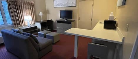 Een hotelkamer met een bank, voetenbankje, televisie, bureau en een schilderij aan de muur.