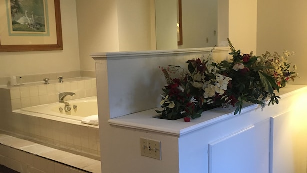A bathroom with a bathtub, a sink, and a mirror above the counter. There is a flower arrangement on the counter.