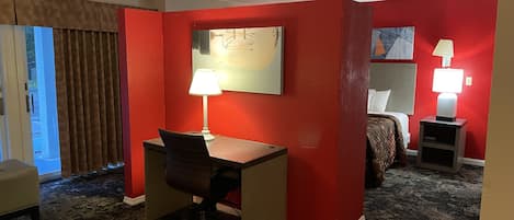 A hotel room with a desk, chair, two bedside lamps, a bed, and a large window with curtains.