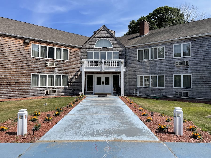 A two-story building with a central entrance, a small balcony, and a pathway leading to the entrance.