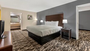 A hotel room with a bed, bedside lamps, a desk with a computer, a mirror, and a door. - Quality Inn & Suites Easley - Greenville (Easley)