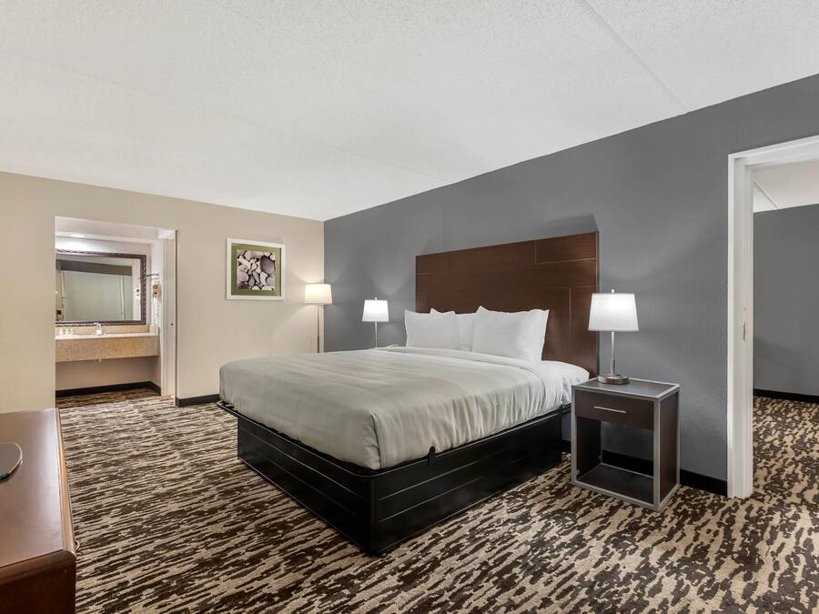 A hotel room with a bed, bedside lamps, a desk with a computer, a mirror, and a door.