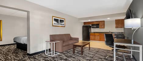 A compact living space with a kitchenette, a sofa, a small table, and a chair.