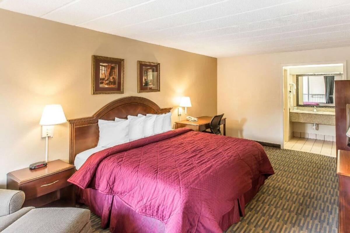 A hotel room with a bed, bedside tables, a desk, a chair, and a bathroom visible through an open door.