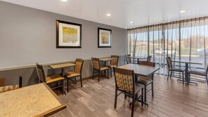 A dining area with tables and chairs, framed artwork on the wall, and a view through large windows. - Quality Inn & Suites Easley - Greenville (Easley)