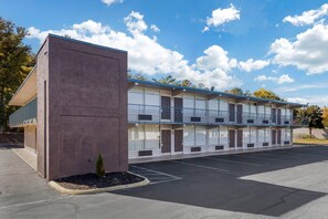 A motel with a two-story structure, a parking lot, and a small landscaped area with a shrub.