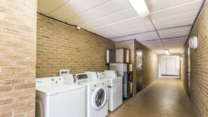 A laundry room with a brick wall, a washing machine, a dryer, and a refrigerator. - Quality Inn & Suites Easley - Greenville (Easley)