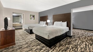 A hotel room with two beds, a desk with a lamp, a TV, and a bathroom with a mirror and sink. - Quality Inn & Suites Easley - Greenville (Easley)