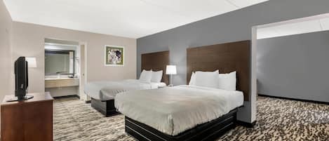 Habitación de hotel con dos camas, un escritorio con lámpara, televisor y baño con espejo y lavamanos.