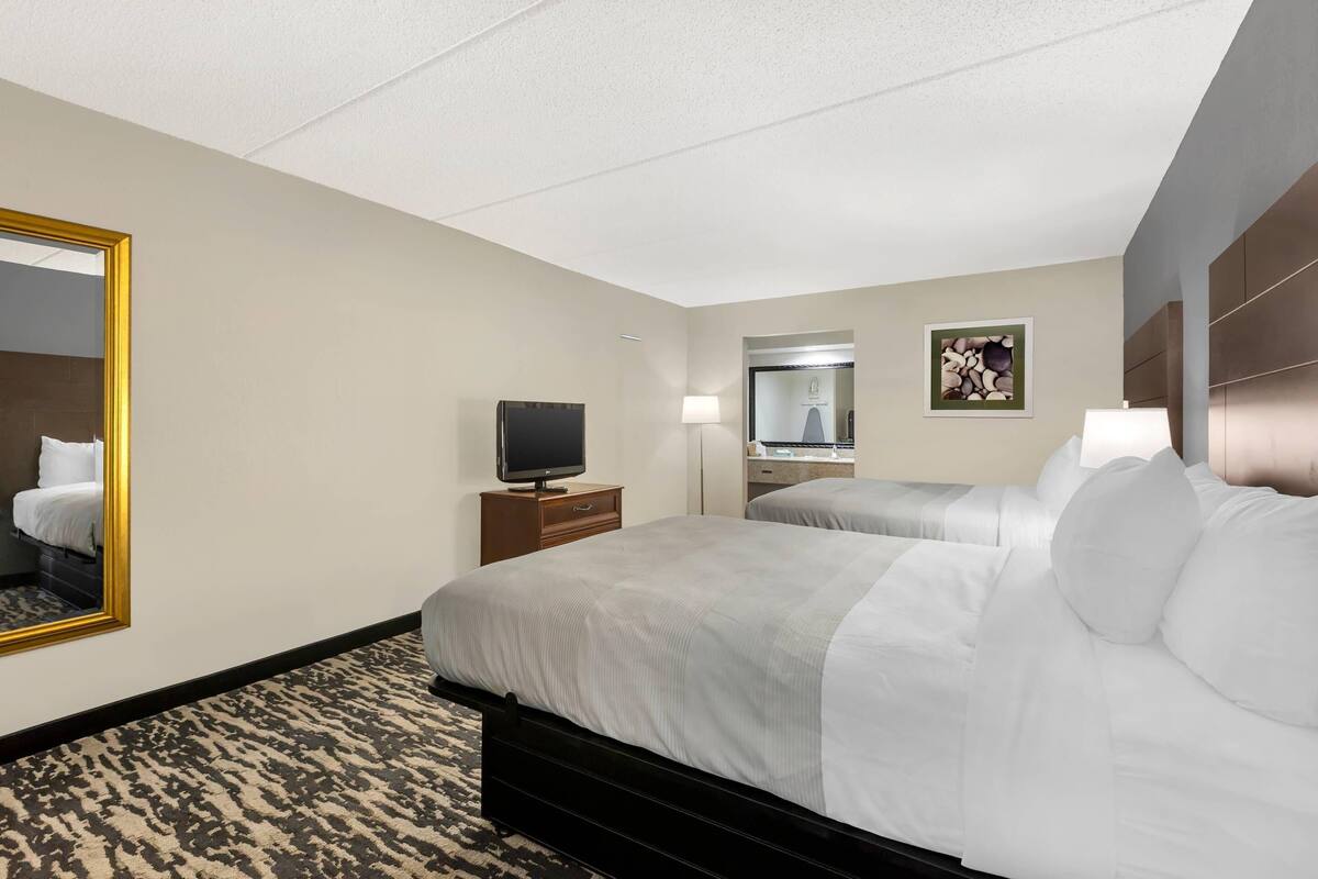 A hotel room with two beds, a TV, a mirror, and a painting on the wall.