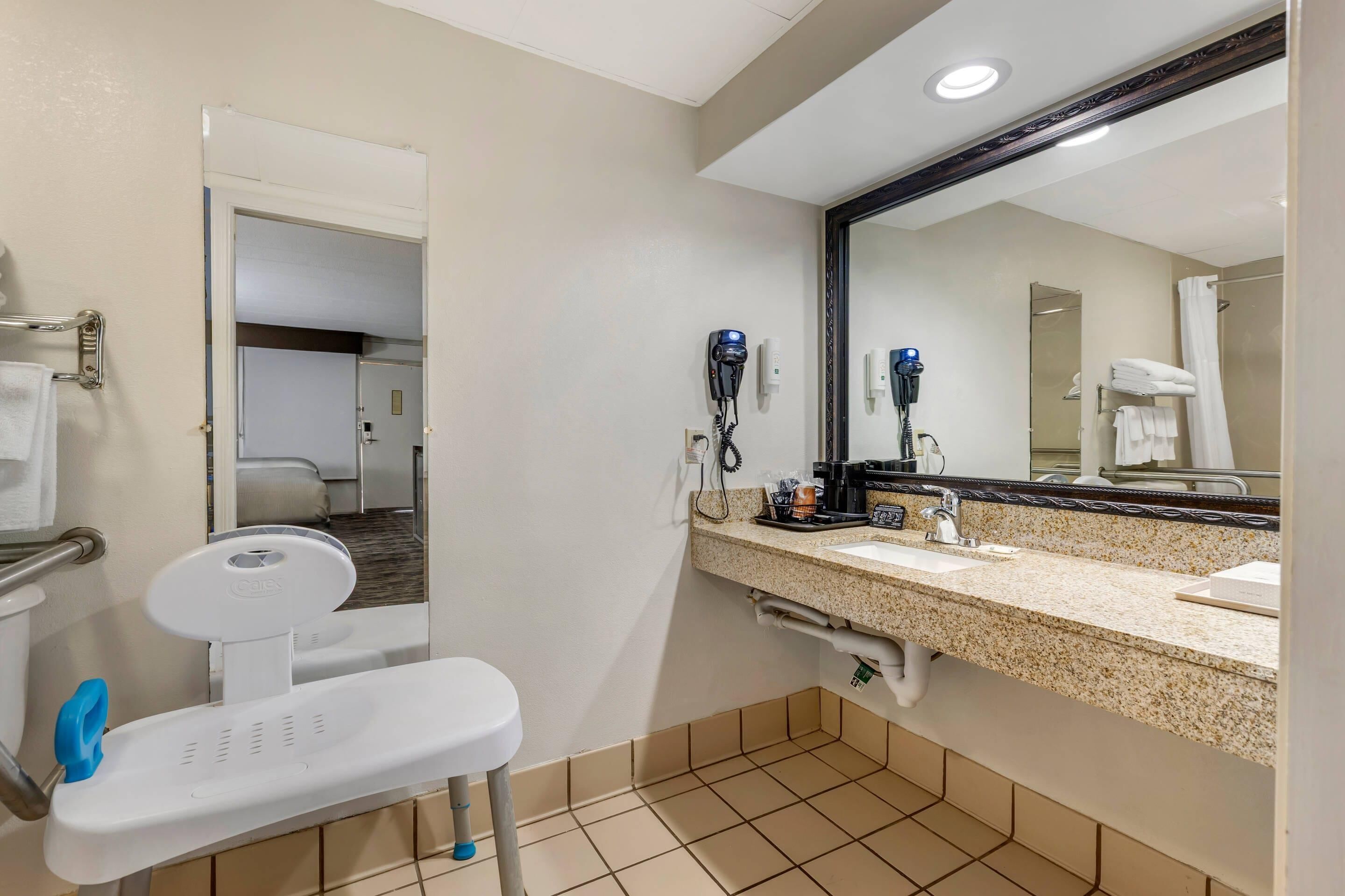 A bathroom with a white toilet, a sink with a mirror, a hairdryer, and a shower area.
