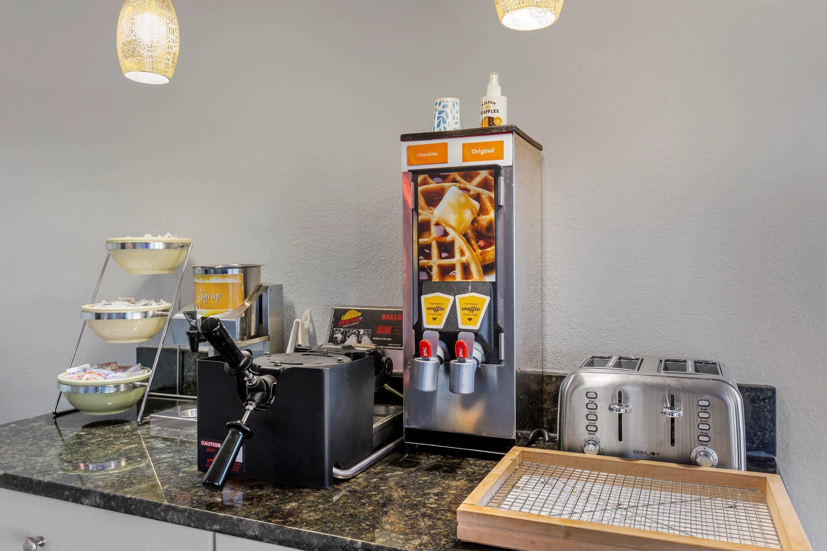 A kitchenette with a waffle maker, toaster, and waffle dispenser.