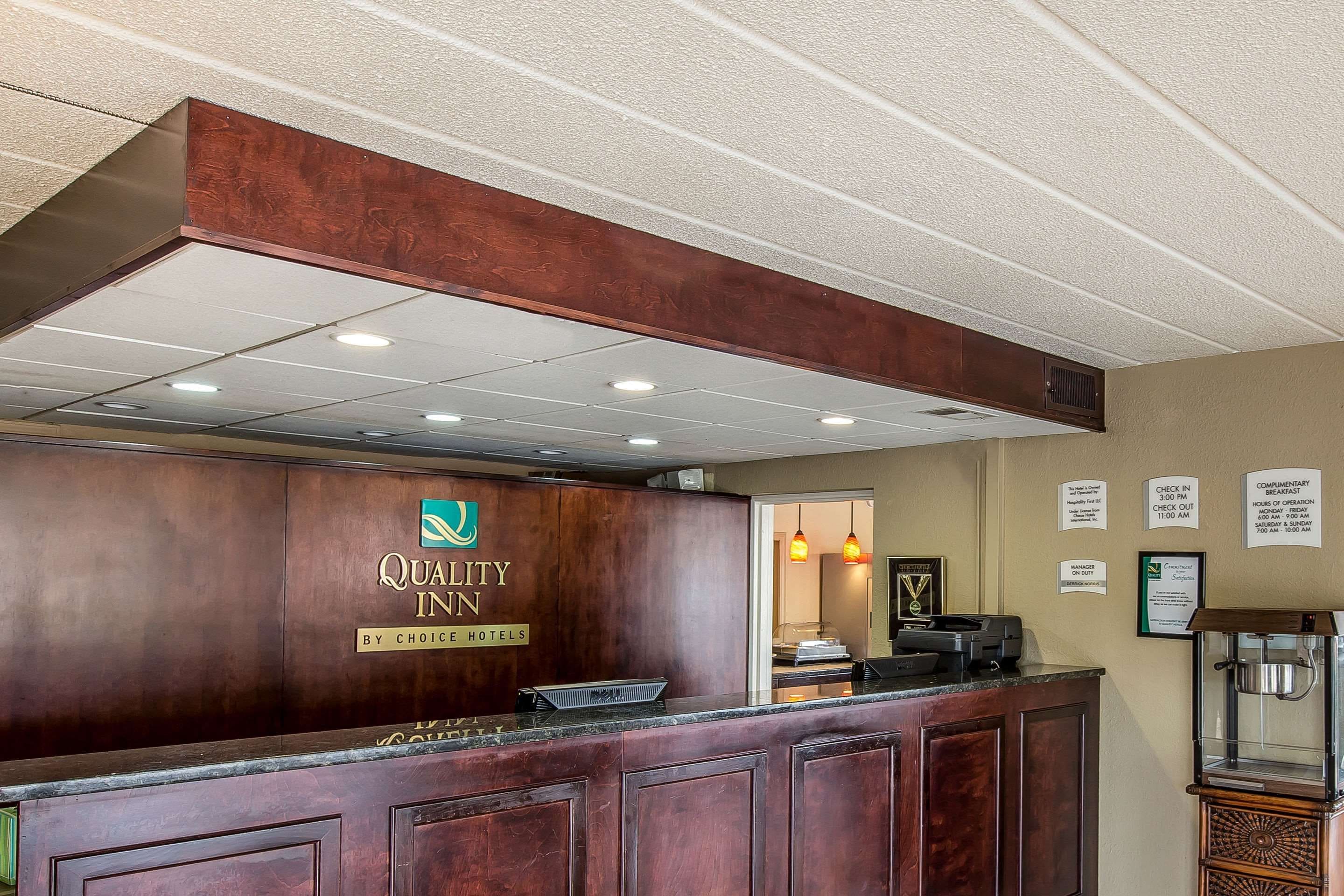 A reception desk with a wooden finish, a sign indicating it's part of the Quality Inn by Choice Hotels, and a check-in counter.