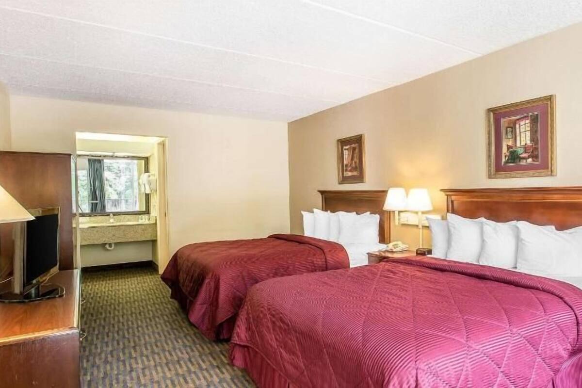 A hotel room with two beds, a window, a mirror, and a door.
