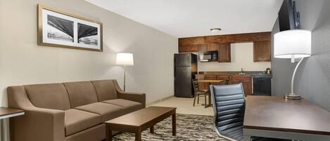 A compact living space with a sofa, a dining table, a kitchen area with a refrigerator and microwave, and a patterned rug.
