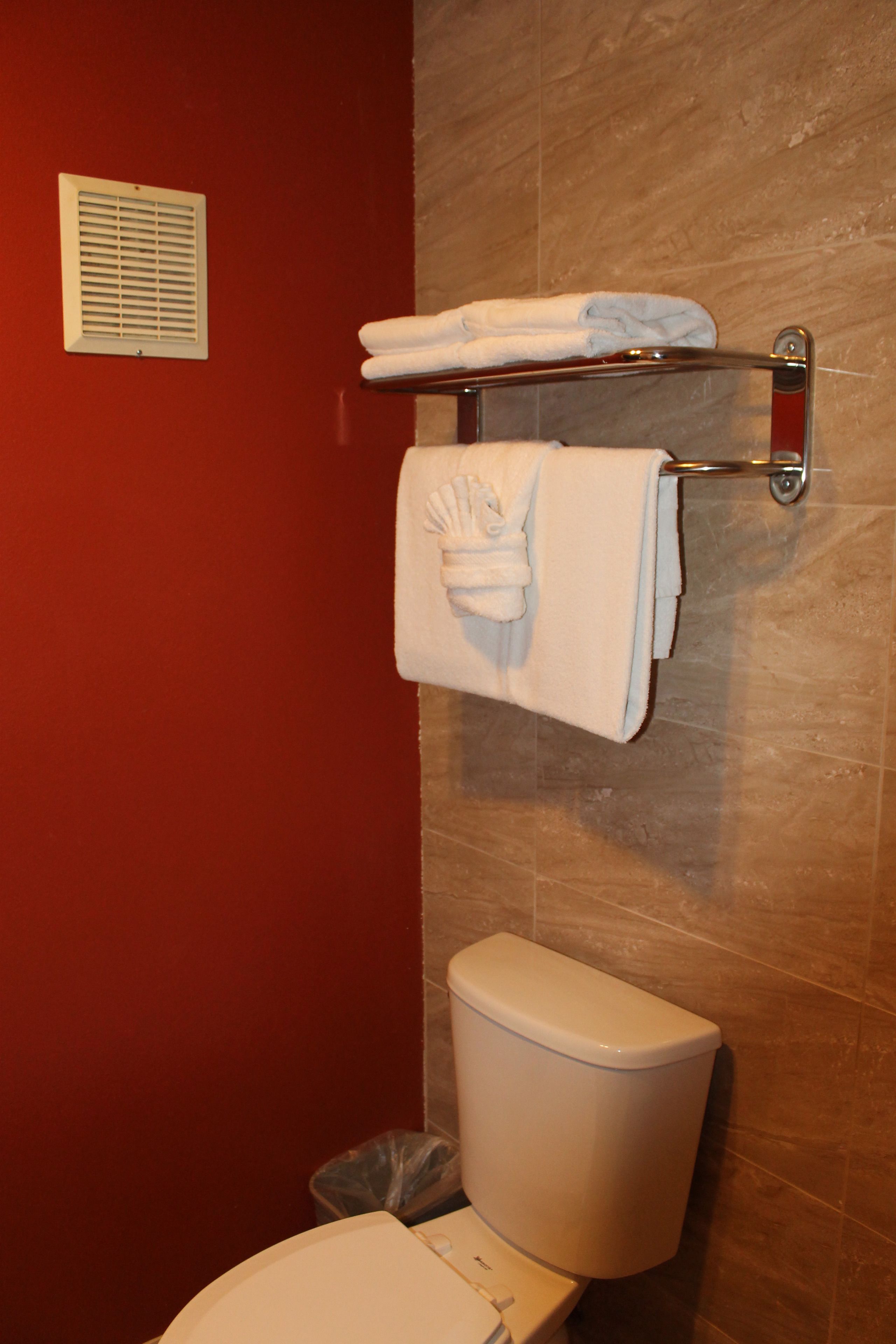 A bathroom with a toilet, a towel rack with towels, and a vent on the wall.