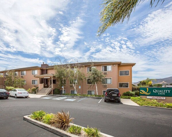 A multi-story motel with a parking lot, a sign indicating availability, and a clear sky.