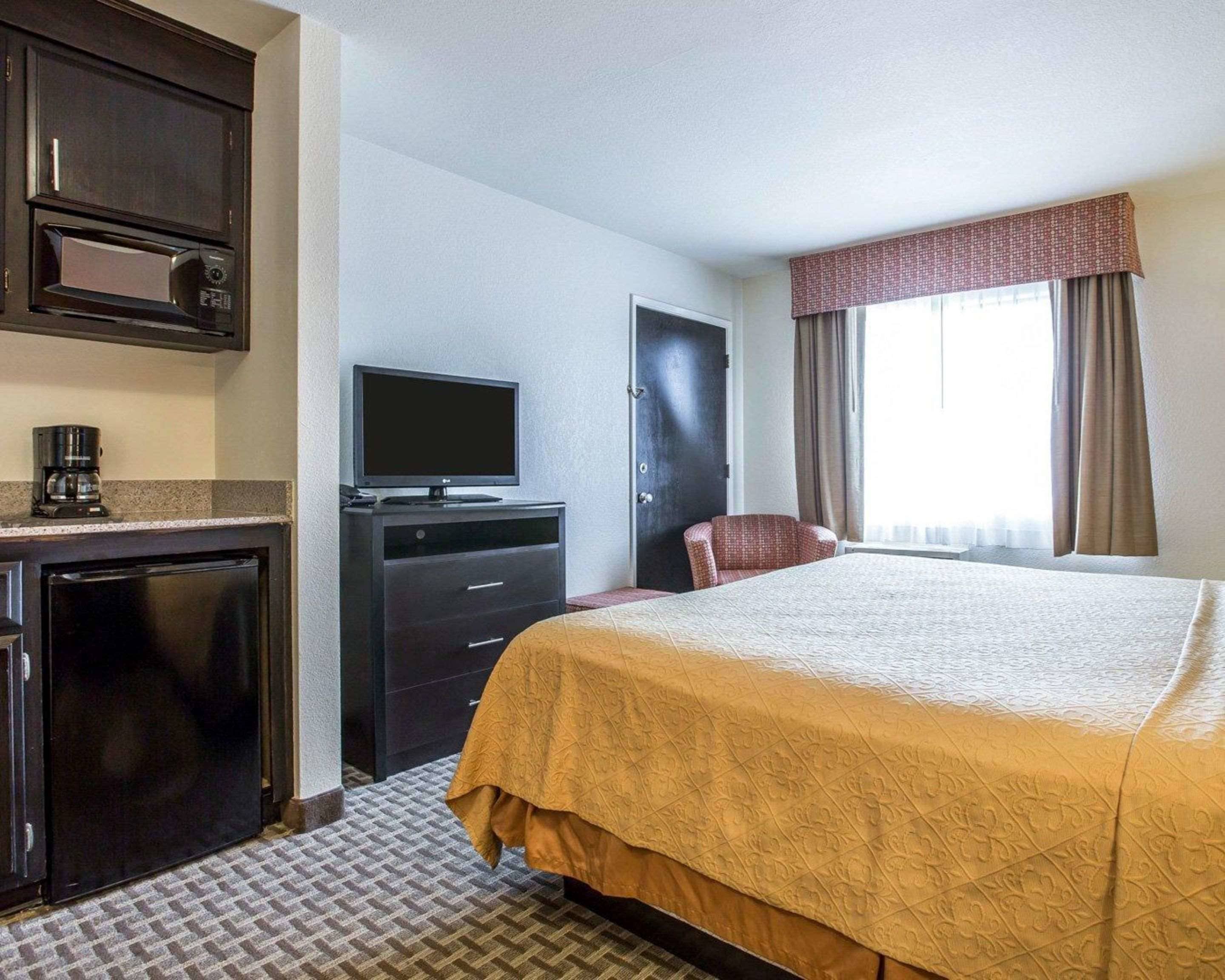 Une chambre d’hôtel comprenant un lit, un bureau avec une télévision, une machine à café et une armoire.