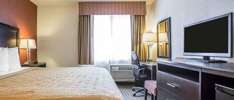 A hotel room with a bed, a desk with a TV, a chair, a desk lamp, and a window with curtains.