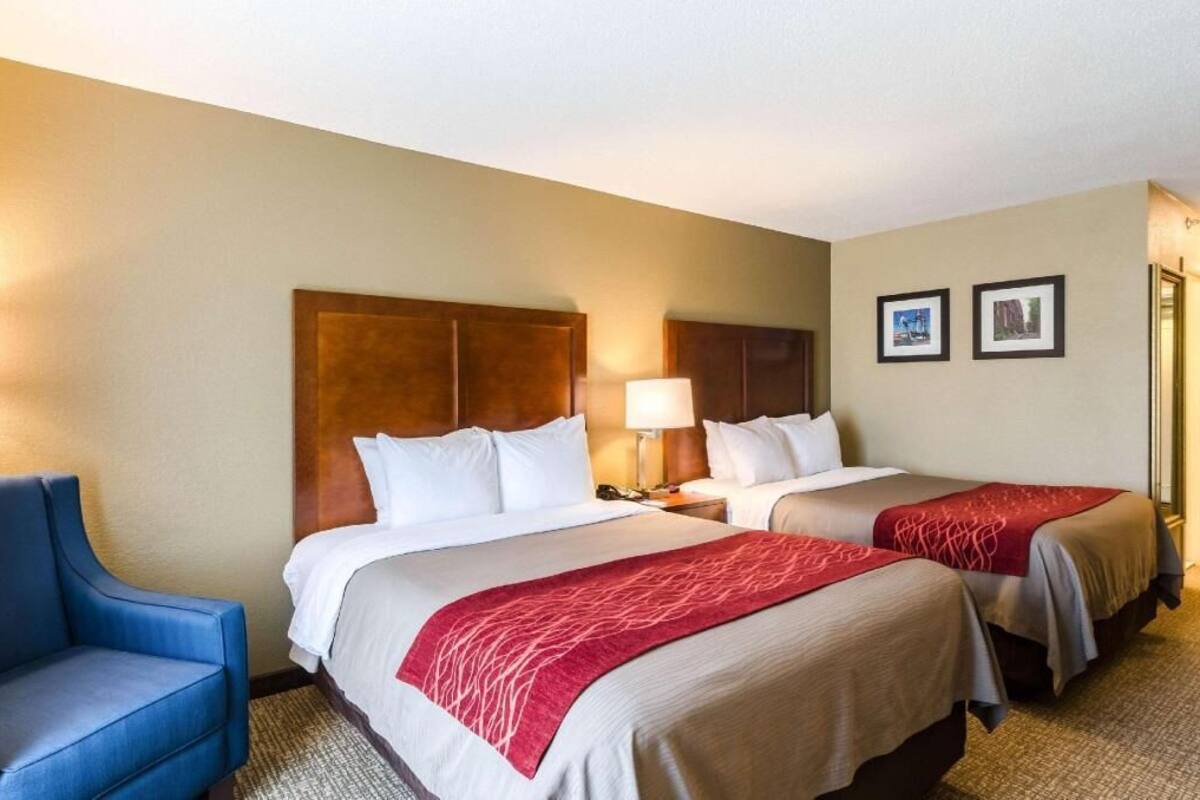 A hotel room with two beds, a blue armchair, and a wooden headboard.