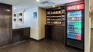 A hotel lobby with a Coca-Cola refrigerator stocked with beverages, snack shelves, and a Comfort Inn sign. - Comfort Inn Randolph - Boston (Randolph)
