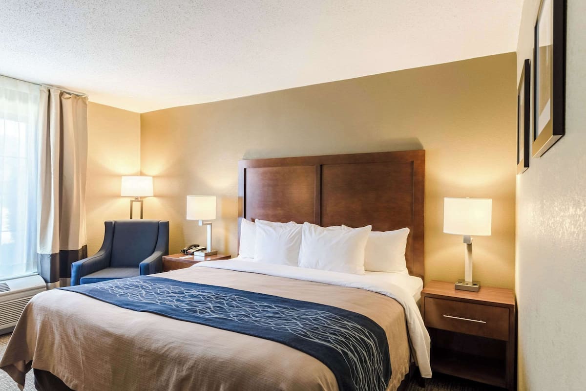 A hotel room with a bed, two bedside lamps, a chair, a nightstand, and a window with curtains.