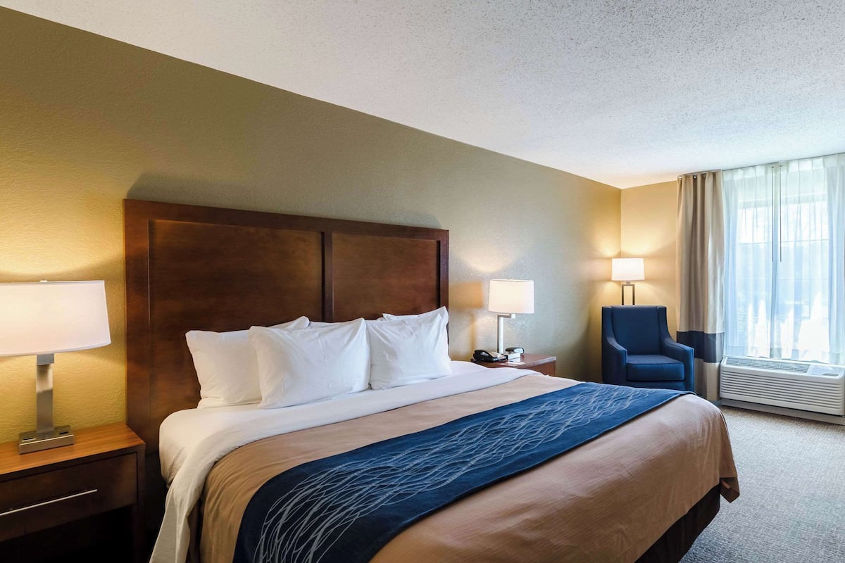 A hotel room with a large bed, two bedside tables, a chair, a desk, and a window with curtains.