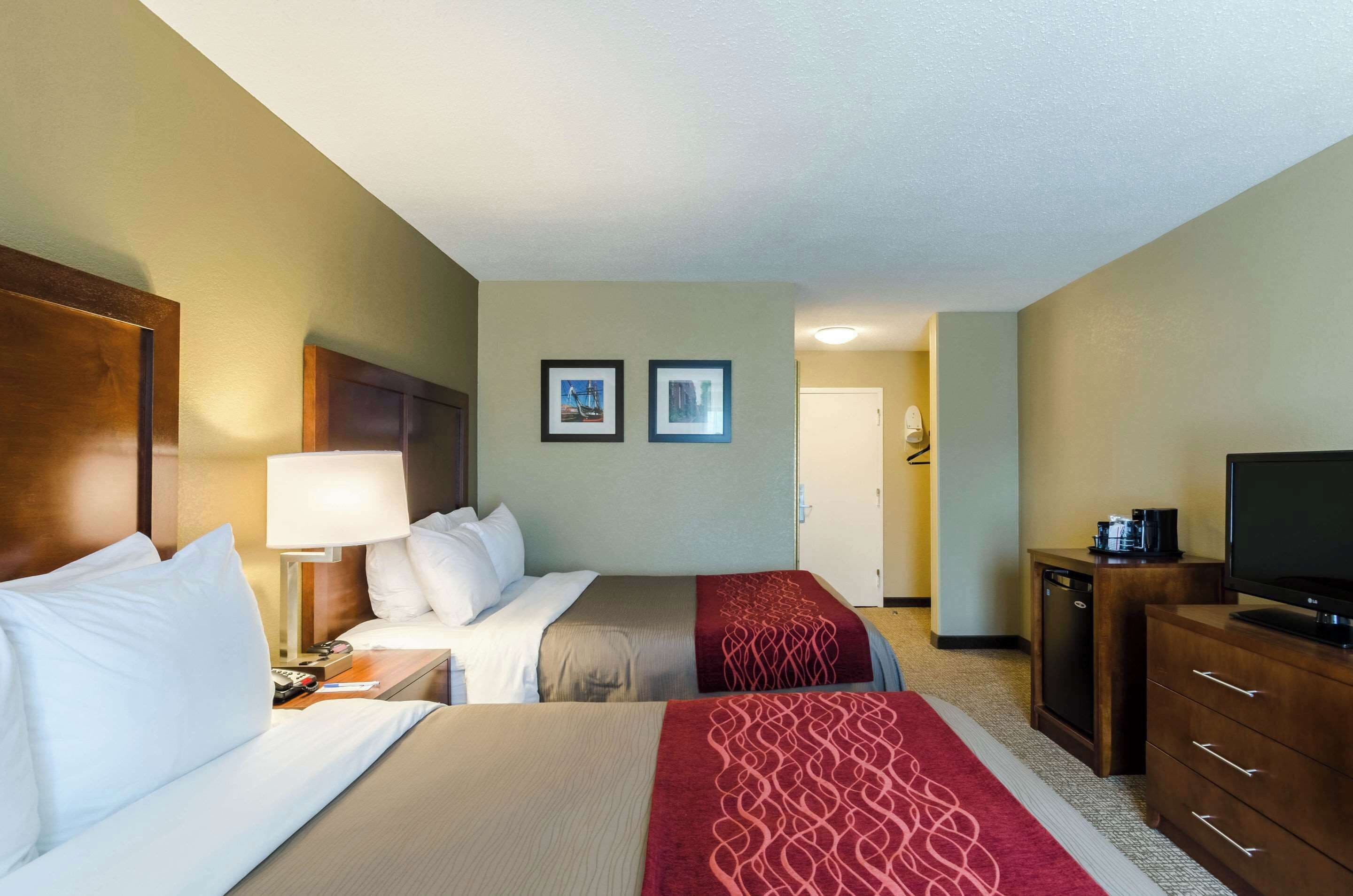 A hotel room with two beds, a desk with a lamp, a television, and a wardrobe.