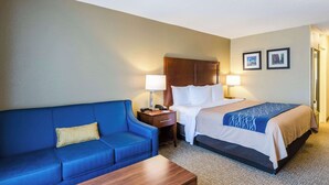 A hotel room with a bed, a blue sofa, a wooden nightstand, and two wall-mounted lamps. - Comfort Inn Randolph - Boston (Randolph)
