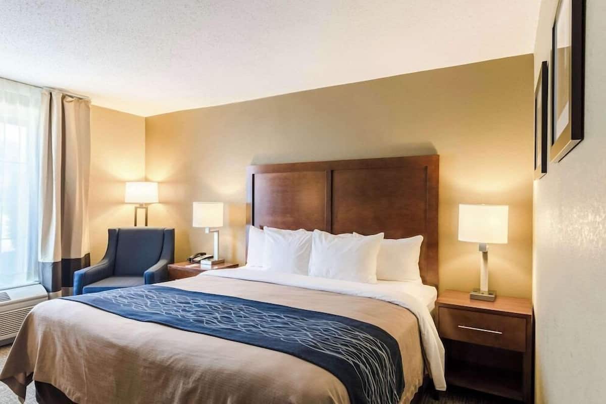 A hotel room with a bed, two bedside tables, a chair, and a window with curtains.
