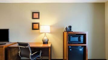 Ein Hotelzimmer mit Schreibtisch aus Holz, einem schwarzen Ledersessel, einer Lampe, einer Mikrowelle und einem Kühlschrank.