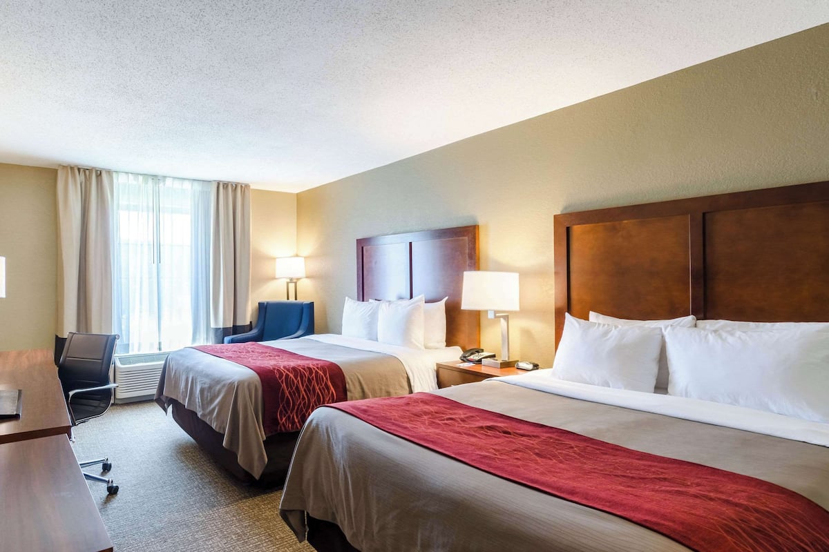 A hotel room with two beds, a desk, a chair, and a window with curtains.