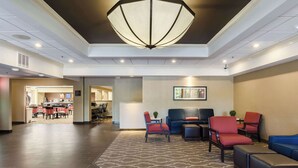 A lobby with a patterned carpet, seating area with red and blue chairs, a large chandelier, and a framed artwork on the wall. - Comfort Inn Randolph - Boston (Randolph)