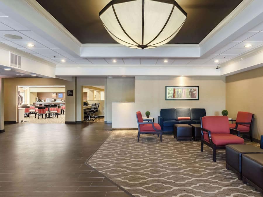 A lobby with a patterned carpet, seating area with red and blue chairs, a large chandelier, and a framed artwork on the wall.