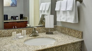Un baño con encimera de granito, lavamanos, espejo y toallero.