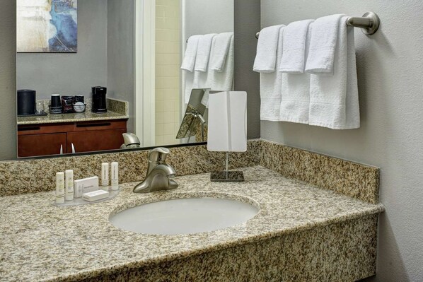 Un baño con encimera de granito, lavamanos, espejo y toallero.