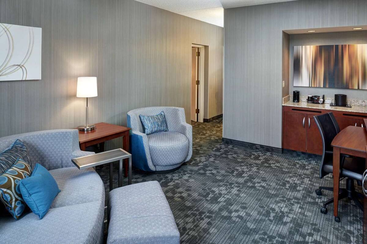 A hotel room with a sofa, armchair, coffee table, desk, and kitchenette.