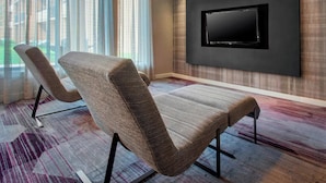Un salon moderne avec un grand téléviseur à écran plat fixé au mur, deux fauteuils confortables et un tapis à motifs.