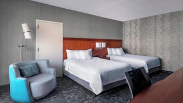 A hotel room with two beds, a seating area with a chair, a desk, and a lamp.