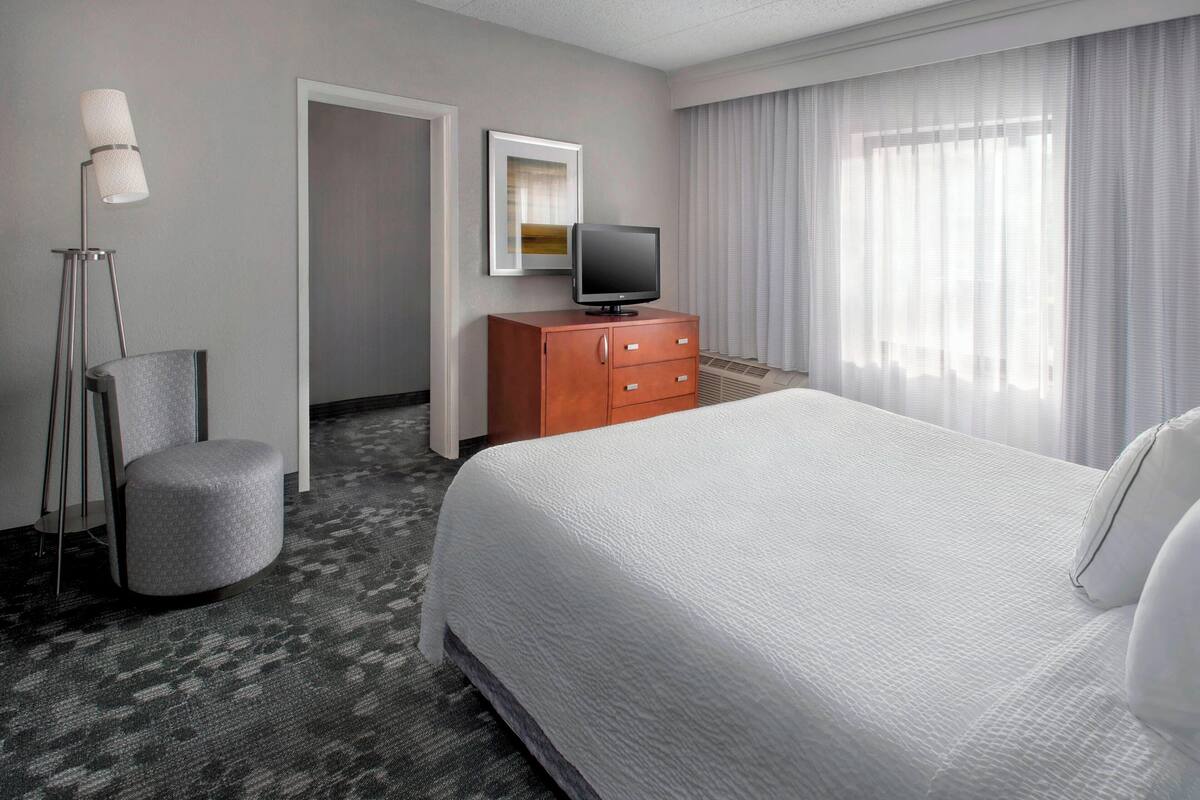 Habitación de hotel con una cama grande, un escritorio con televisor de pantalla plana, una silla, un aparador y una lámpara de pie.