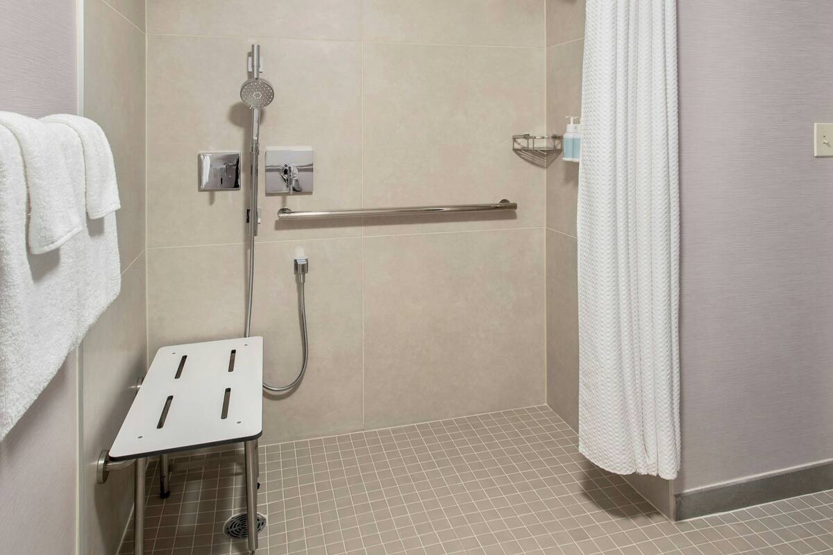 Un área de ducha moderna con un cabezal de ducha de mano, una barra de apoyo y una toalla blanca colgada en la pared.