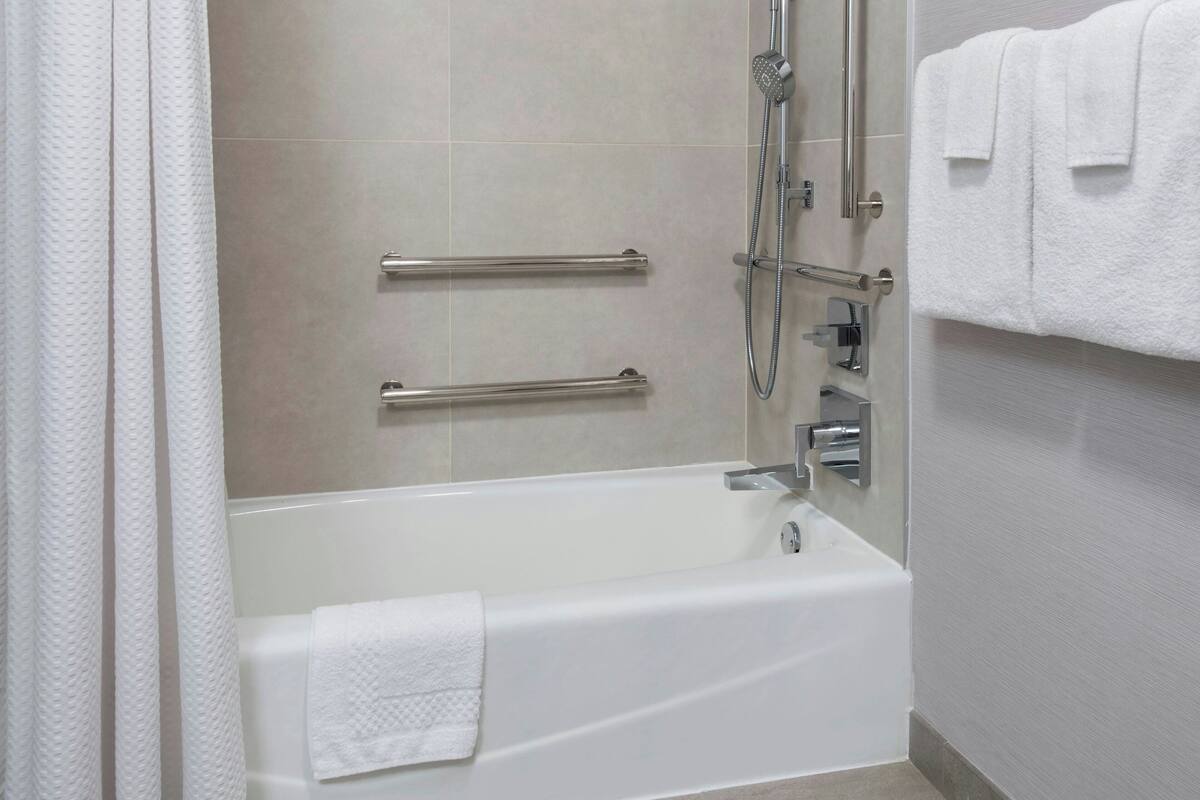 Un baño moderno con bañera, barras de apoyo y ducha.