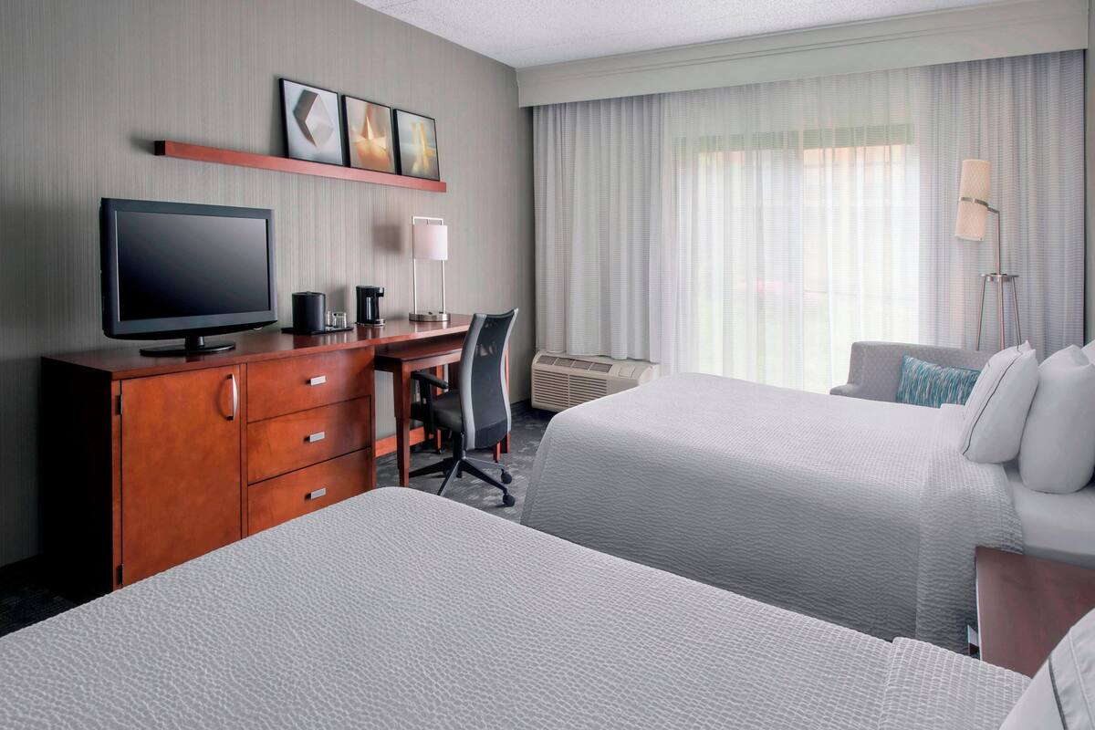 Una habitación de hotel con dos camas, un escritorio con computadora, televisor y cafetera.