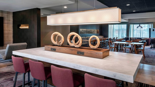 Un espace bar moderne doté d’un comptoir en marbre, de tabourets de bar rouges et d’un élément décoratif central en bois original.