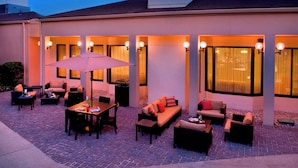 Un espace extérieur aménagé en terrasse, avec des coins salon comprenant des canapés et des tables, ainsi qu’un grand parasol.