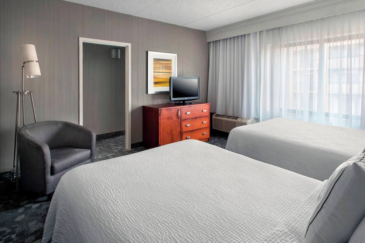 Habitación de hotel con dos camas, un televisor sobre una cómoda de madera, una lámpara y una puerta.
