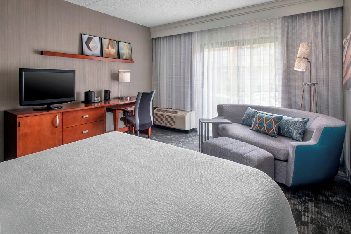 Habitación de hotel con una cama grande, un escritorio, un televisor de pantalla plana, un sofá y una lámpara.