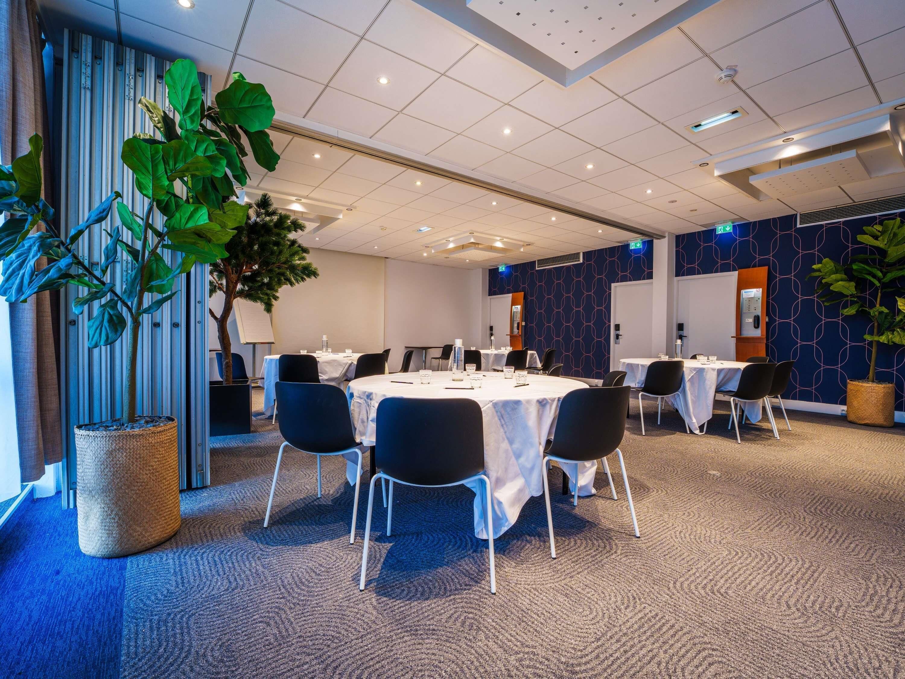 A conference room with round tables, chairs, and potted plants.
