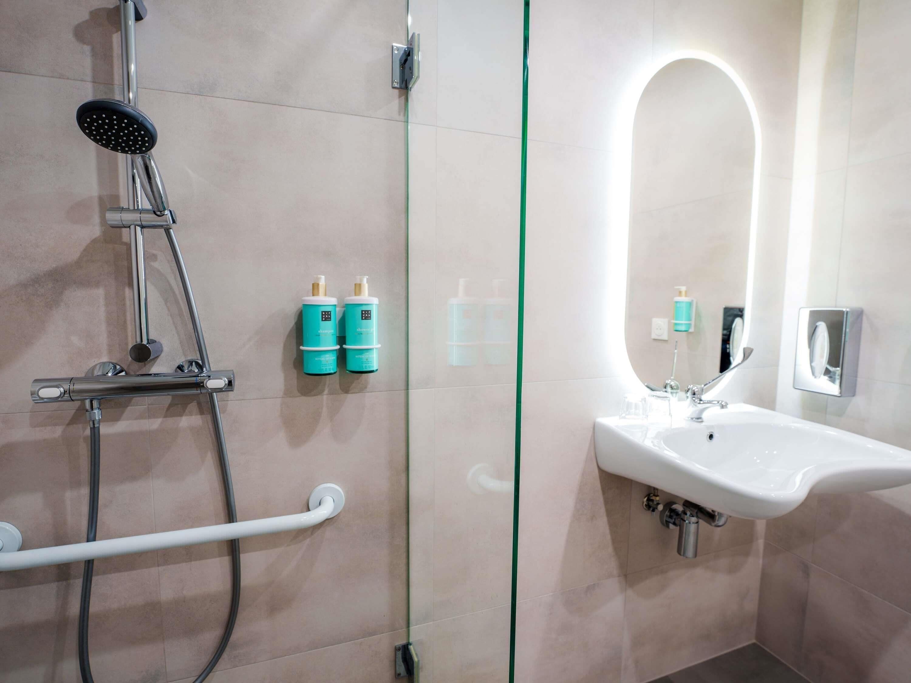 A modern bathroom with a glass-enclosed shower, a white sink, and two bottles of shampoo on the wall.