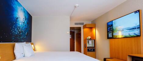 A hotel room with a large bed, a TV, a desk, and a painting on the wall.